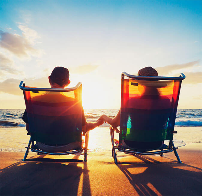 Couple sitting in chairs overlooking the ocean while holding hands.
